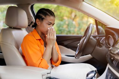 Arabada otururken hapşıran ya da burnunu silen Afrikalı Amerikalı bir kadın. Hasta görünüyor, doku tutuyor, muhtemelen mevsimsel alerji ya da soğuk algınlığı geçiriyor.