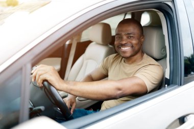Arabanın şoför koltuğunda otururken camdan gülümseyen kendinden emin Afrikalı Amerikalı adam. Yakışıklı siyahi adam, pozitif enerjiyle yola çıkmaya hazır. Yakın çekim.