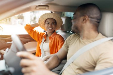 Neşeli siyah çift birlikte arabaya biniyor, yolculuğun tadını çıkarıyorlar, tatile çıkıyorlar, arabada sohbet ederken birbirlerine sıcakkanlılıkla gülümsüyorlar.