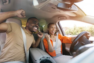 Neşeli siyah çift arabada birlikte kutluyor, Afrikalı Amerikalı erkek ve kadın araba sürerken sevinçten kollarını kaldırıyor ya da heyecanlı bir yolculuk deneyimi sırasında, yakın plan