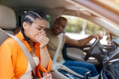 Genç siyahi kadın midesi bulanırken erkek araba sürüyor, endişeli erkek arkadaşı endişeli ve rahatsız edici bir yolculuk anında yardım etmeye çalışıyor.