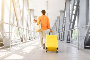 Havaalanında elinde pasaport ve biniş kartı olan bir kadının arka görüntüsü. Güven dolu bir maceraya doğru yol alırken, boşluğu kopyala