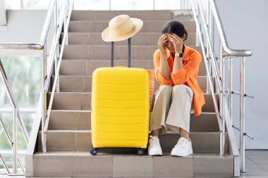 Stresli siyah kadın gezgin elinde bavulla merdivenlerde oturuyor. Havaalanında kaçırılan ya da beklenmeyen uçuş sayısı, kopyalama alanı