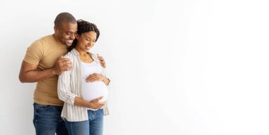 Afrika kökenli Amerikalı çifti seven bir adam, hamile karısını arkadan kucaklayan, hem gülümseyen, hem de bebeklerinin gelişini bekleyen bir adam..