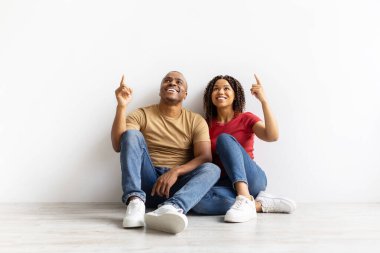 Mutlu Afro-Amerikan çifti yere oturmuş, gülümsüyor ve yukarıdaki boş alana bakıyor, ilanınız için bedava bir yer.