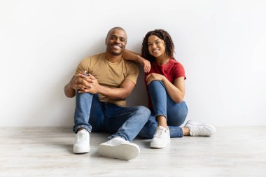 Beyaz duvara yaslanmış, rahat Afro-Amerikan bir çift, kameraya gülümseyen mutlu siyah adam ve kadın, gündelik giysiler içinde, kopyalama alanı