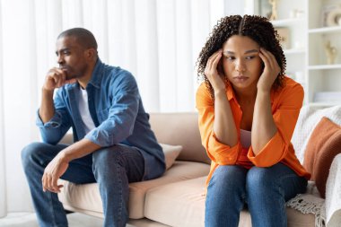 Stresli Afrikalı Amerikalı çift tartışmadan sonra ayrı oturuyorlar. İkisi de gözlerini kaçırıyorlar. Duygusal uzaklık ve ilişki gerginliği gösteriyorlar.