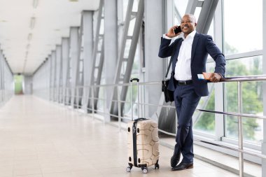 Bavullarıyla ayakta duran ve havaalanında cep telefonuyla konuşan kendinden emin bir zenci işadamı. Profesyonel yaşam tarzı, seyahat, küresel iletişim ve modern ulaşım, kopyalama alanı