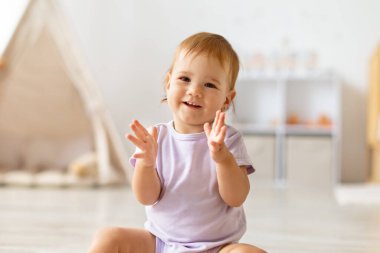 Gülümseyen bebek yerde otururken el çırpıyor. Yaşam tarzı mutluluk, oyun, öğrenme, masumiyet, aile sevgisi, annelik sevgisi ve bağ kurma..