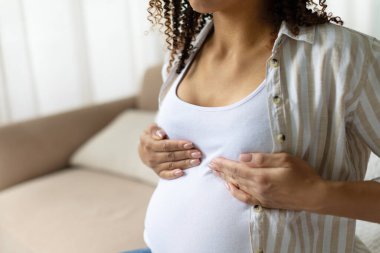 Hamile Afrikalı Amerikalı kadının gömleğin üzerinden göğüslere dokunması, vücut değişimi, hassasiyet ve doğum dönemi boyunca sağlık hizmetleri.