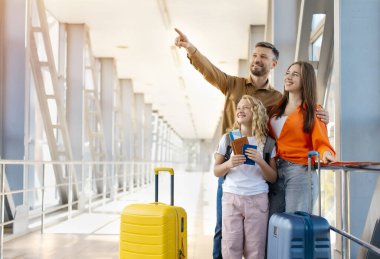 Havaalanında bavulları ve pasaportları olan mutlu beyaz aile, yön gösteriyor ve gülümsüyor, neşeli yaşam tarzı gösteriyor, bağ kuruyor ve tatil ayrılışı heyecanı, kopyalama alanı