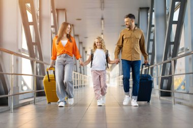 Kızıyla birlikte havalimanı terminalinde el ele tutuşup mutlu bir seyahat ve tatil yolculuğunun tadını çıkaran beyaz bir aile.