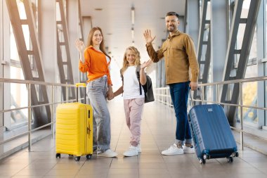 Kızı havaalanı terminalinde el sallayan, gülümseyen ve bavullarını tutan, neşeli ayrılışı, seyahat yaşam tarzını ve mutlu anları sembolize eden beyaz bir aile.
