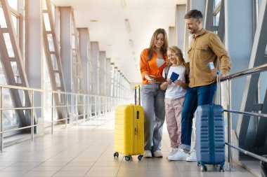 Havaalanında bavulları ve pasaportlarıyla gülümseyen beyaz aile, ayrılmadan önce belgeleri birlikte kontrol ediyorlar, bağ, seyahat yaşam tarzı ve mutluluğu sembolize ediyorlar.