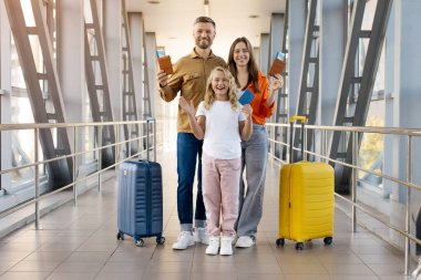 Üç kişilik gülümseyen beyaz aile havaalanında pasaport ve biniş kartlarını gösteriyor, mutlu gidiş, yaşam tarzı, bağlanma ve uluslararası tatil seyahatlerini sembolize ediyor