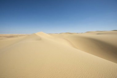 Mısır 'ın ıssız, ıssız batı çölünün manzarası. Mavi gökyüzü arka planında büyük kum tepeleri var.