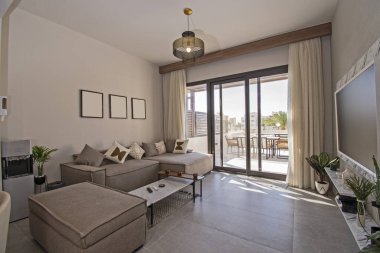 Lüks tropikal tatil dairesindeki oturma odası salonu açık plan tasarımı ve geniş balkon terası ile döşenmiş iç tasarım dekorunu gösteriyor.