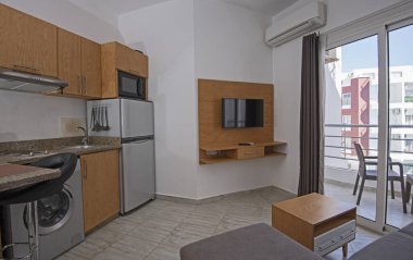 Lüks apartmandaki oturma odasının oturma odası ev dekorasyonunu gösteriyor. Açık mutfak ve balkonla döşenmiş.