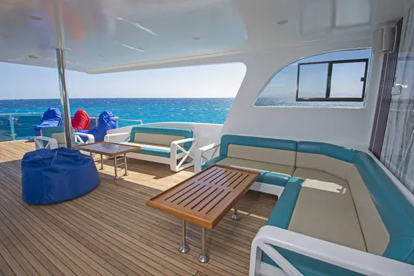 大型豪华游艇的细长船尾木制主甲板 有沙发桌和热带海景背景 图库图片