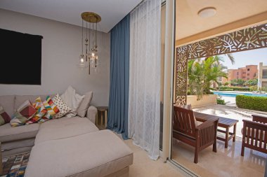 Lüks apartmandaki oturma odası salonu teras ve havuz manzaralı iç tasarım dekorasyonunu gösteriyor.