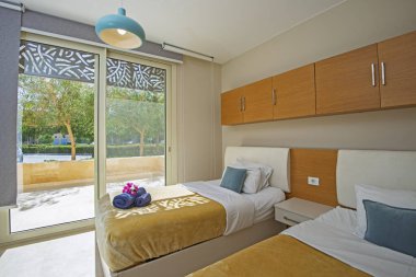 Lüks mobilyaların iç dizayn dekorasyonu ev odası mobilyaları ve bahçe manzaralı ikiz yatakları gösteriyor.