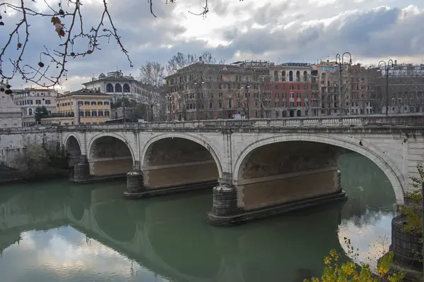 Roma 'daki Tiber nehri üzerindeki eski taş kemerli yol köprüsü bulutlu gökyüzü ile Europen şehir merkezi