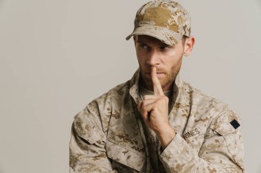 Üniformalı beyaz bir asker beyaz arka planda izole edilmiş sessizlik hareketi yapıyor.