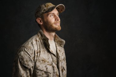 Üniformalı beyaz bir asker gülümsüyor ve siyah arka planda tek başına bir kenara bakıyor.