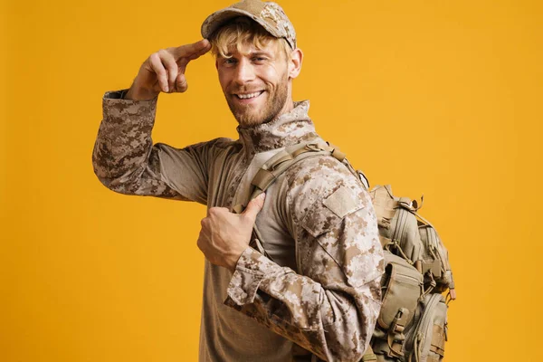 White military man wearing uniform smiling and saluting isolated over yellow background