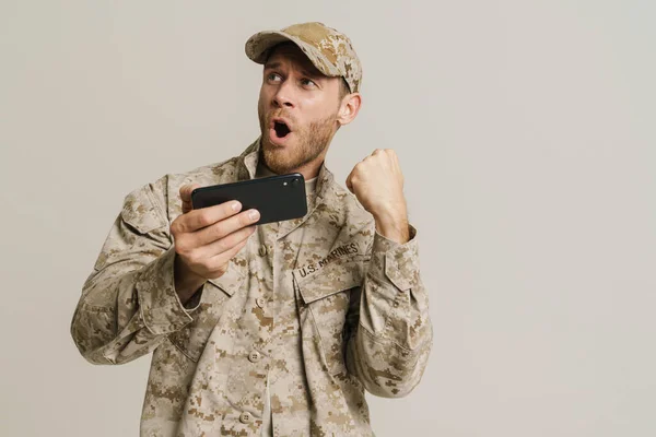 stock image White military man gesturing while playing game on cellphone isolated over white background