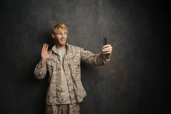 黒の背景に隔離された携帯電話で自慰行為をしながら手を振る白人軍人 — ストック写真