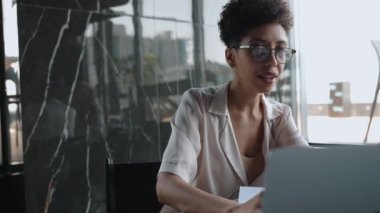 Ciddi Afrikalı kıvırcık saçlı kadın bilgisayarla ofiste konuşuyor.