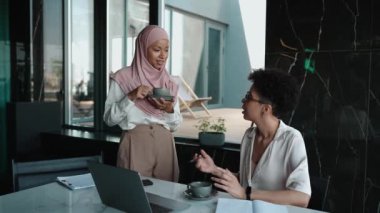 İki tane çok ırklı Müslüman ve Afrikalı kadın ofiste dizüstü bilgisayara bakıp konuşuyorlar.