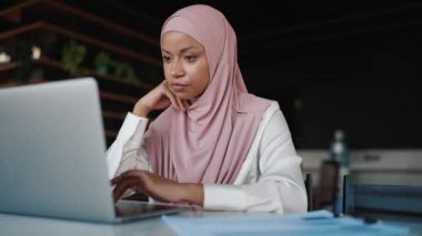 Ofiste dizüstü bilgisayarla çalışan konsantre Müslüman Afrikalı kadın.