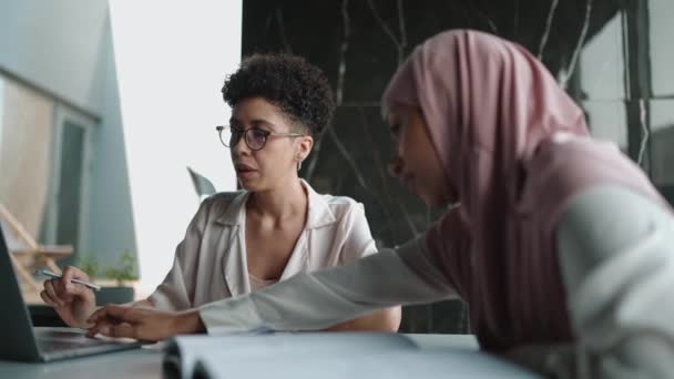 两名自信的多族裔穆斯林和非洲妇女在办公室里一边聊天一边看手提电脑 — 图库视频影像