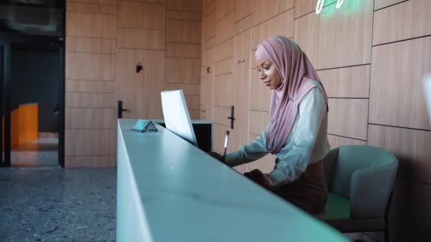 Pozytywna Muzułmańska Recepcjonistka Stoi Przy Recepcji Patrzy Monitor Hotelu — Wideo stockowe