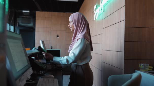 Entuzjastyczna Muzułmańska Recepcjonistka Stoi Przy Recepcji Rozmawia Przez Telefon Hotelu — Wideo stockowe