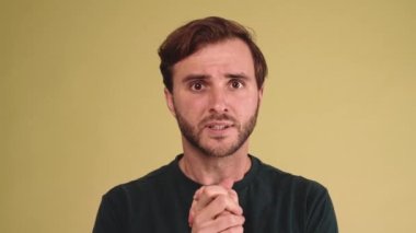 Tişört giyen endişeli esmer genç adam sarı stüdyoda üzülüyor.