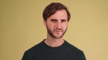 Hoşnutsuz esmer genç adam sarı stüdyoda sessizlik jesti yapıyor.