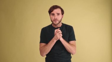 Tişört giyen esmer bir genç adam sarı stüdyodaki kameraya seviniyor.