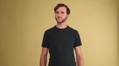 Gülümseyen esmer adam etrafa bakıyor ve sarı stüdyoda kameraya el sallıyor.