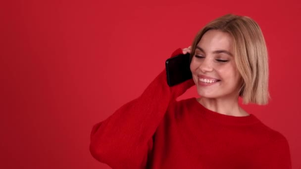 笑顔ブロンド女性身に着けています赤いセーターを身に着けています電話でザ赤スタジオ — ストック動画