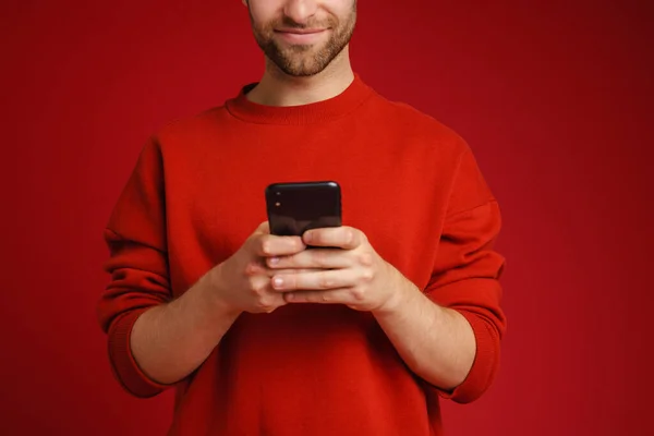 年轻的毛茸茸的男人 穿着毛衣 面带微笑 用红色背景隔离的手机 — 图库照片