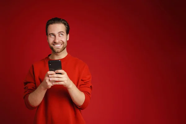 年轻的毛茸茸的男人 穿着毛衣 面带微笑 用红色背景隔离的手机 — 图库照片