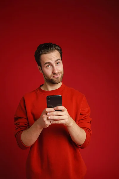 Young Perplexed Man Looking Camera Using Cellphone Isolated Red Background — Stock Photo, Image