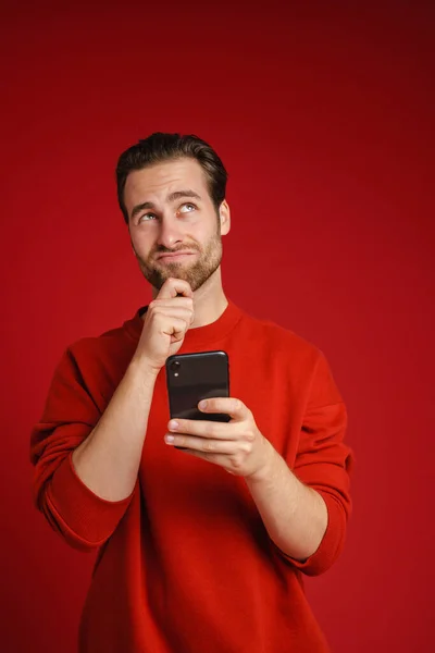 Young Perplexed Man Looking Camera Using Cellphone Isolated Red Background — Stock Photo, Image