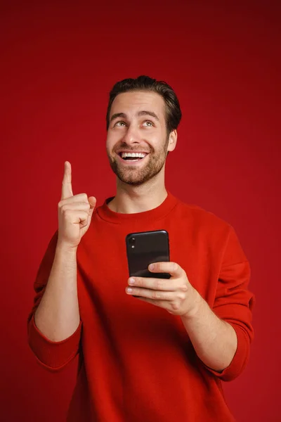 年轻的毛茸茸的男人指着手指向上 用红色背景隔离的手机 — 图库照片