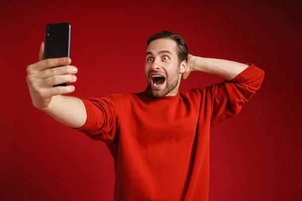 在红色背景下 年轻人在手机上自拍时表现出惊讶的表情 — 图库照片