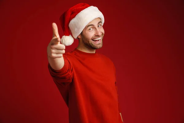 Молодой Щетина Человек Рождественской Шляпе Указывая Пальцем Камеру Изолированы Красном — стоковое фото