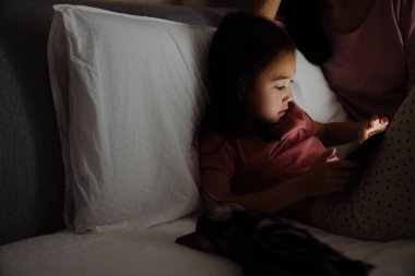Asian girl using tablet computer while sitting on bed at home